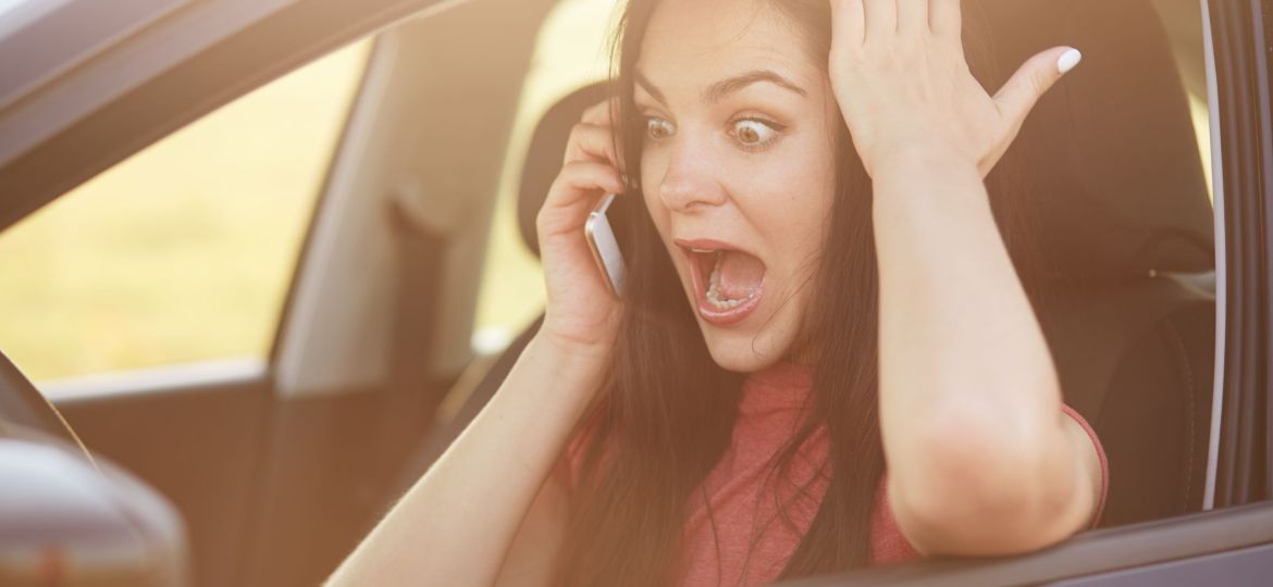 Shocked beautiful young female driver doesnt know how to repair car, makes call to husband via cellular, stares with surprisement and fear, keeps jaw dropped, poses in automobile. Omg concept