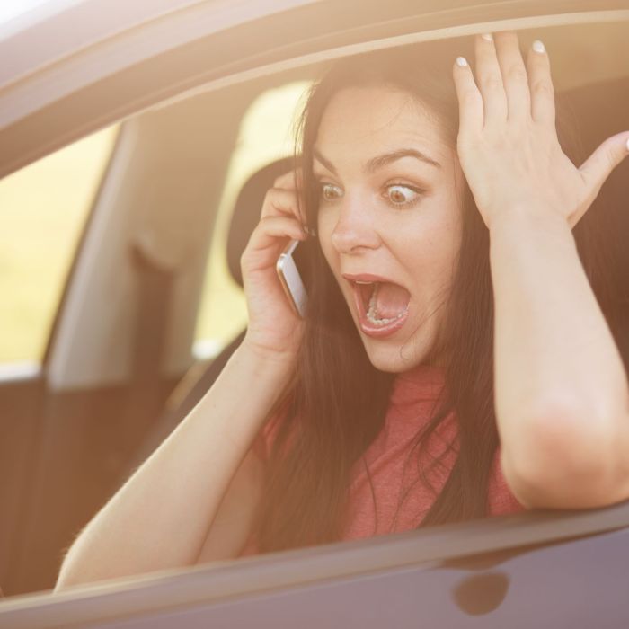 Shocked beautiful young female driver doesnt know how to repair car, makes call to husband via cellular, stares with surprisement and fear, keeps jaw dropped, poses in automobile. Omg concept
